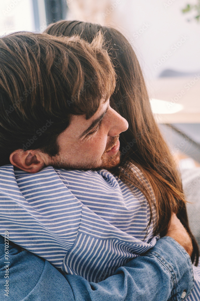 Obraz premium Smiling couple sitting on sofa at home hugging each other happy. Concept of love and happiness