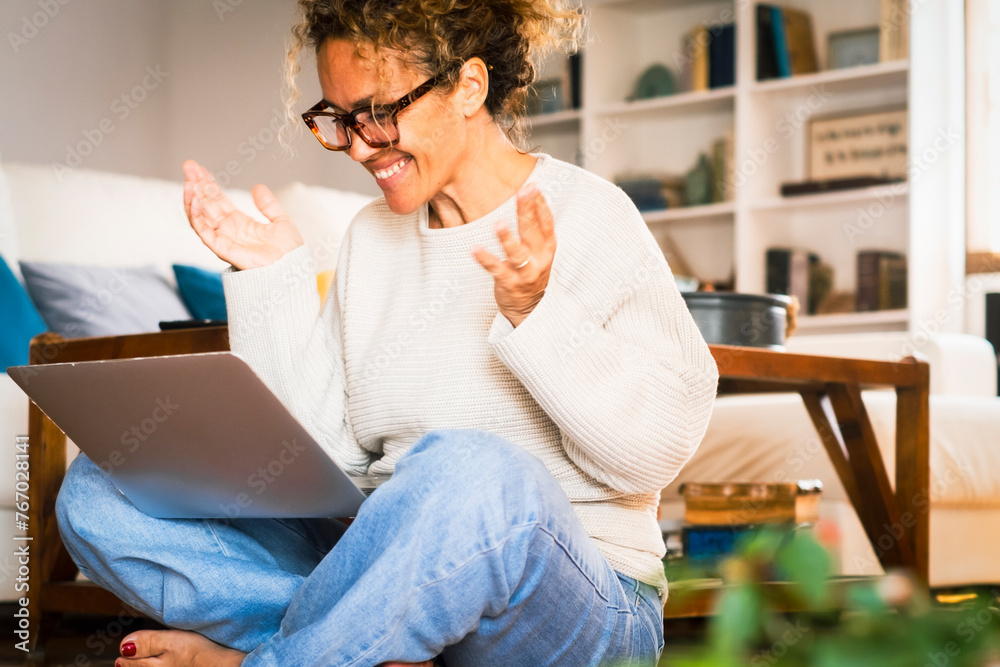 One excited happy woman doing video call using laptop at home sitting barefoot on the floor. Female gesturing with hands in front of a computer and videocall conference. Online meeting dating website