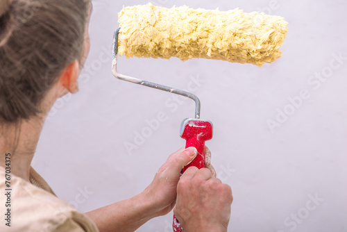 A close-up shot of anonymous woman hands using a yellow roller brush for painting her house, embodying the DIY spirit photo