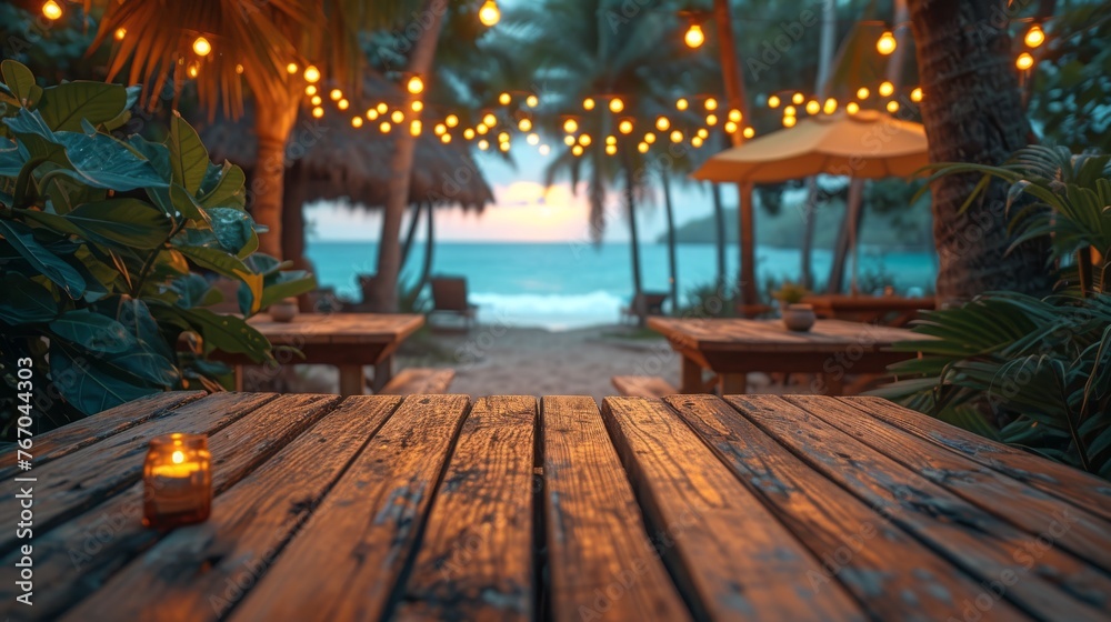   A wooden table with a candle illuminating it, situated on a beach surrounded by palm trees and overhead lights - obrazy, fototapety, plakaty 