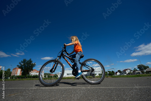 girl in an orange sweater rides a bicycle