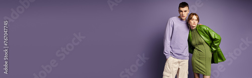 loving couple in vibrant clothes posing together on purple background and looking at camera, banner