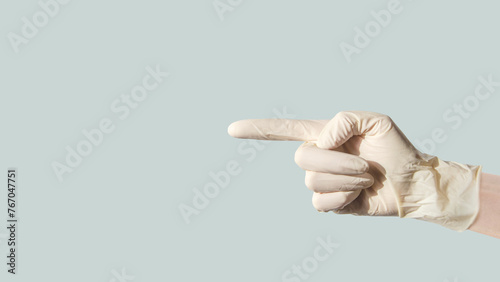 female hand in latex glove, pointing her index finger to side at an empty space on blue background photo