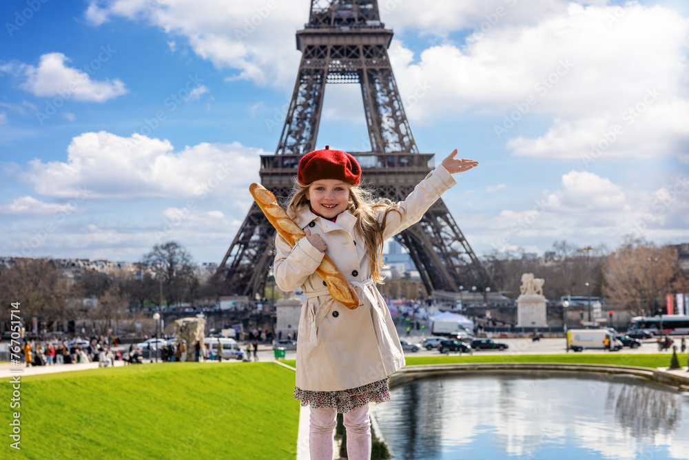 Fototapeta premium Paris travel concept with a cute blonde girl holding a french baguette bread in front of the Eiffel Tower