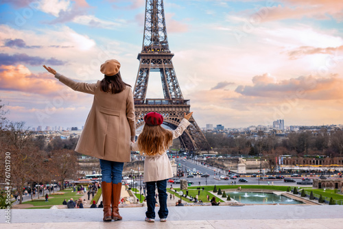 A happy mother and daughter on vacation stand in the front of the famous Eiffel Tower in Paris, France