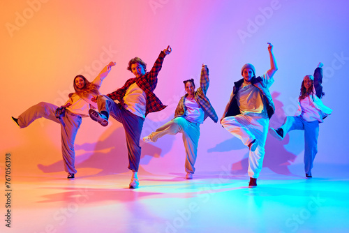 Dynamic performance of five talented dancers in motion, dancing modern dance against gradient studio background in neon light. Concept of modern dance style, hobby, active lifestyle, youth culture