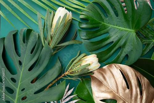 Tropical leaves and flowers over green background, summer background with copy space