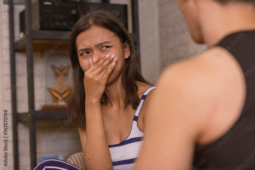 Φωτογραφία A young Asian woman expresses disgust towards her boyfriend's tactless, obscene and gross comments while sitting on a living room sofa