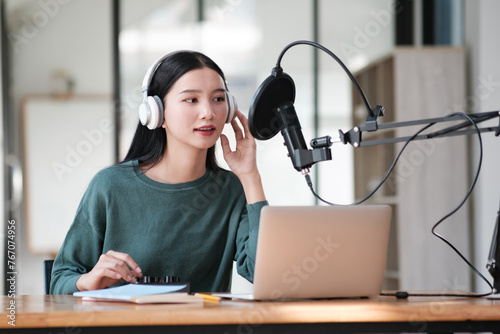 A woman wearing headphones is sitting at a desk with a laptop and a microphone