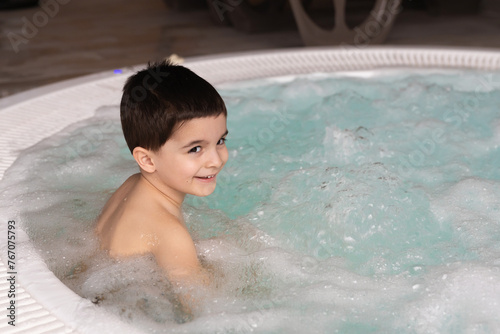 Boy sitting in the warm bubbling water jacuzzi. Happy kid relaxing in spa