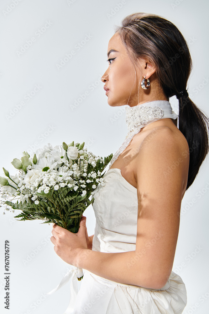 profile of young bride in elegant outfit with white flowers bouquet on light background