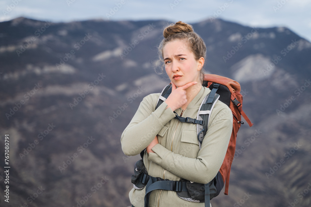 Young hiker woman with backpack looking at camera and thinking, feeling doubtful and confused, makes decision in mind, serious-looking girl processing situation in mind, Hmm, let me think, empty space