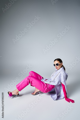 Fashionable woman in pink gloves, leather pants and chic sunglasses lying on grey background