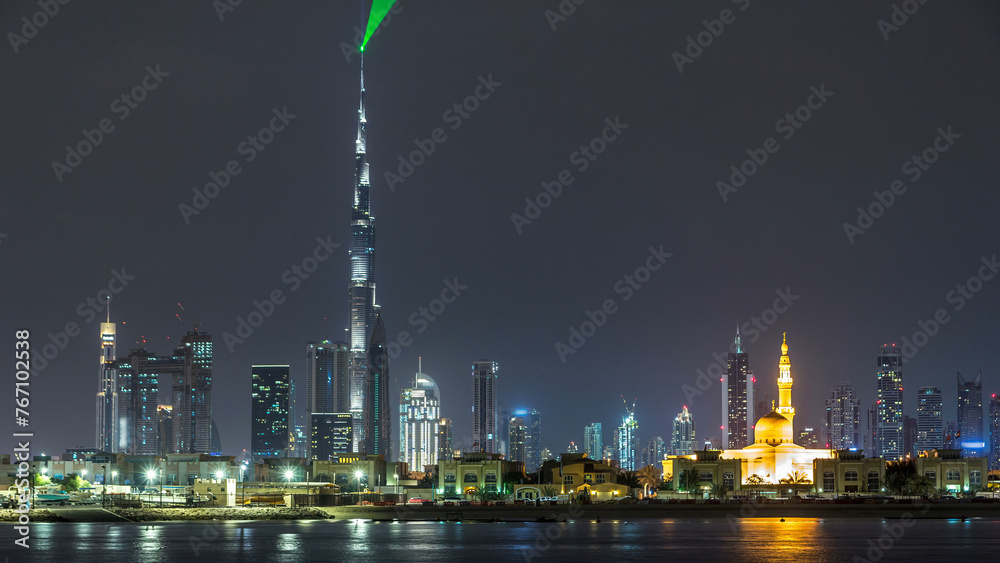 Modern Dubai city skyline timelapse at night with illuminated skyscrapers over water surface