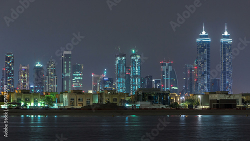 Modern Dubai city skyline timelapse at night with illuminated skyscrapers over water surface