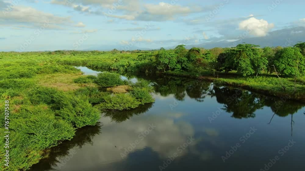 Flying above the river in Costa rica jungle forest, close to Jaco town. Drone view of a river flowing into the ocean. Blue sky and clouds reflection in to the water. 4K wide angle. Flying above the river in Costa rica jungle forest, close to Jaco town. Drone view of a river flowing into the ocean. Blue sky and clouds reflection in to the water. 4K wide angle.
