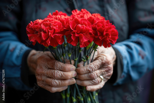 An elderly person's hands gently holding a bouquet of vibrant red carnations