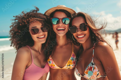 Three women wearing bikinis and sunglasses are smiling for the camera. Scene is happy and carefree, as the women are enjoying their time at the beach © Nataliia_Trushchenko