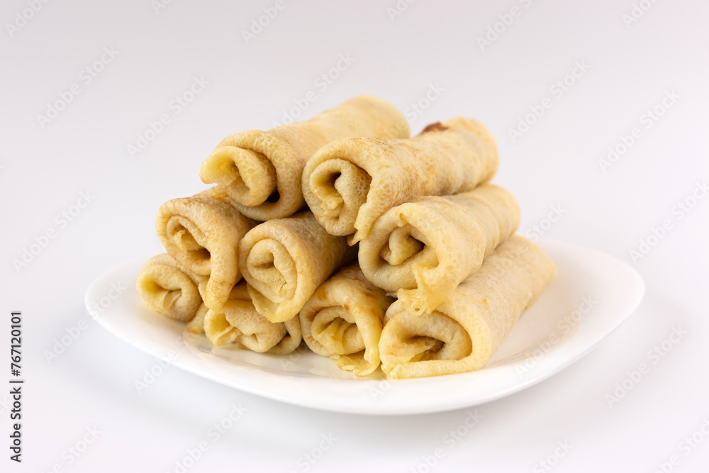 Freshly baked wrapped pancakes with filling on a plate on a white background.