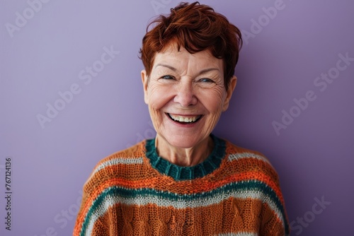 Portrait of a smiling senior woman in a sweater on a purple background