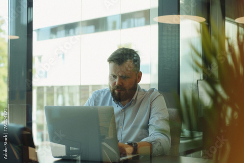 Middle aged business man executive financial investor sitting at desk using laptop. Busy professional businessman ceo manager working on computer corporate technology in modern office. Portrait.