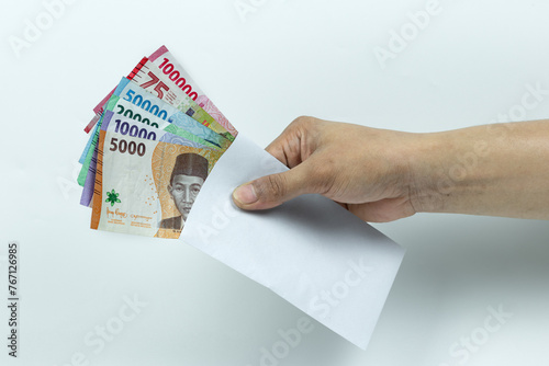 Asian man's hand holding Stack of Rupiah or IDR banknotes inside white envelope on white background