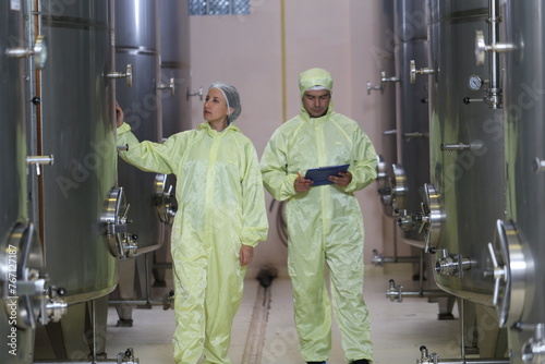 .woman winemaker and business owner wearing sterile clothing, holding a notebook, checking air pressure to control the quality and temperature of the fermented tanks in a winemaking factory.