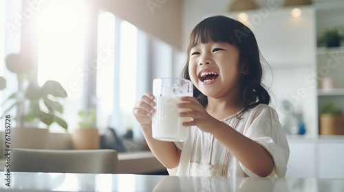 Little Asian Girl Drinking Milk in Bright Modern Kitchen