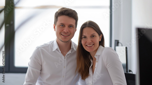 Homem e mulher de camisa branca sorrindo na frente do computador no escritorio