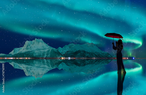 Northern lights in the sky over Tromso, Norway - Young girl in white dress holding red umbrella and walking on the calm water