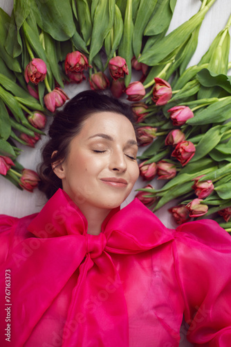 Beautiful brunette woman in a red dress lies on the floor with red tulips for a holiday.There are flowers around the head. large portrait of a man light from a window