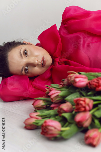 Beautiful brunette woman in a red dress lies on the floor with red tulips for a holiday. fresh bouquet of flowers with a pleasant smell of love and happiness. 