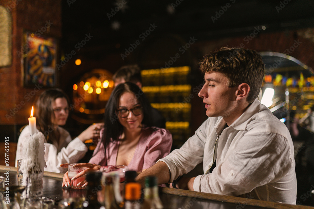 Young people communicate at meeting in restaurant. Smiling lady in elegant dress attracts attention of guy in contemporary restaurant