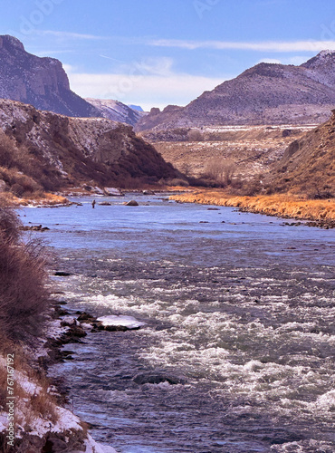 Fisherman upstream in fast flowing Shoshone River has a view of mountains leading into Yellowstone National Park from Cody, Wyoming in February winter.
