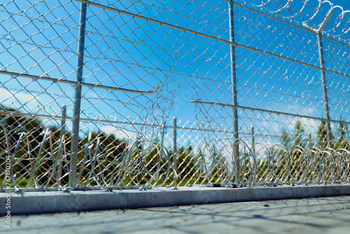 Damaged Metallic Chain-Link Fence with Razor Wire Against a Clear Blue Sky photo