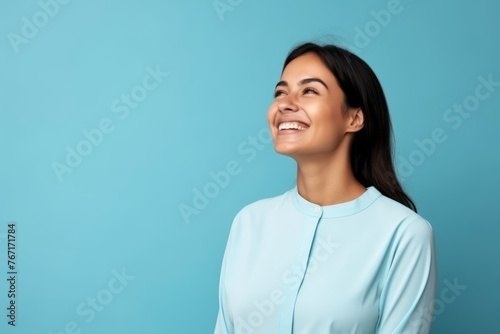 Portrait of a happy young woman laughing on blue background with copy space