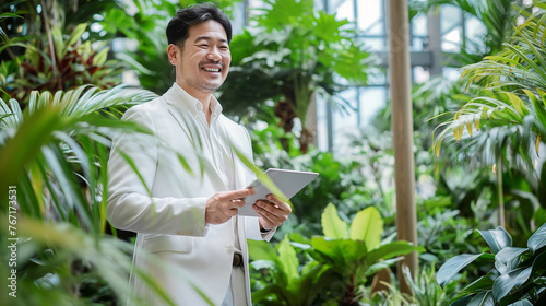 Homem japones vestindo um terno branco segurando um tablet em um escritório cheio de plantas - Conceito de sustentabilidade