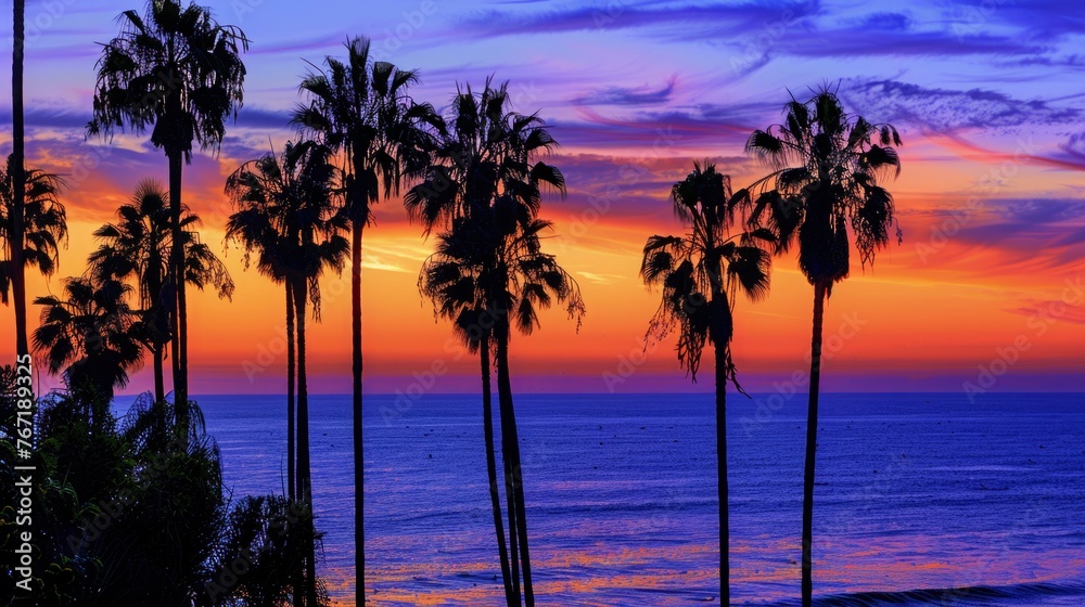 Obraz premium A beautiful sunset over the ocean with palm trees in the background. The sky is a mix of orange and purple hues, creating a serene and calming atmosphere
