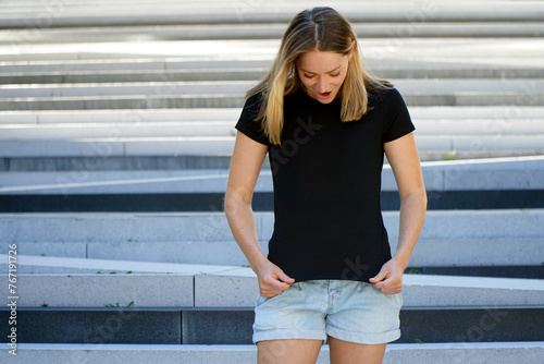 Amazed young blonde woman wearing black t-shirt with copy space or text space for print or design	
