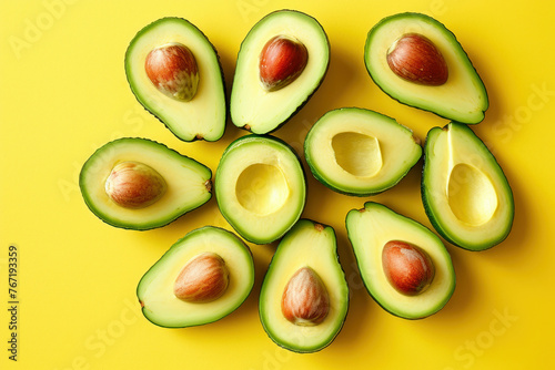 Fresh ripe avocados sliced in half on a vibrant yellow background, arranged in a top view flat lay style