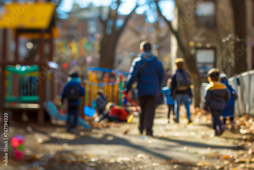 A tilt-shift image of a teacher in a schoolyard during recess, the teacher in sharp focus while the background is blurred.