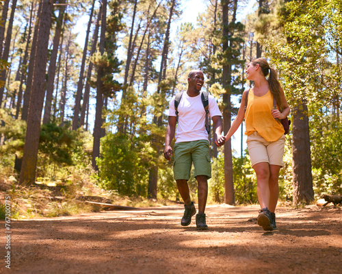 Fototapeta Naklejka Na Ścianę i Meble -  Loving Young Couple Wearing Backpacks Holding Hands Hiking Along Trail Through Countryside