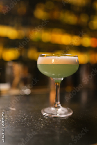 Green colored alcoholic cocktail stands on black surface. Elite beverage in glamorous glass made with addition of alcohol background lights of pub photo