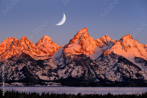 Sunrise on Teton Mountain Range in Wyoming Alpen Glow Orange and Pink on Rugged Mountains with Crescent Moon photo