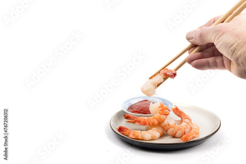 A hand picking up a cooked peeled shrimp with chop sticks to dip into seafood sauce isolated on white