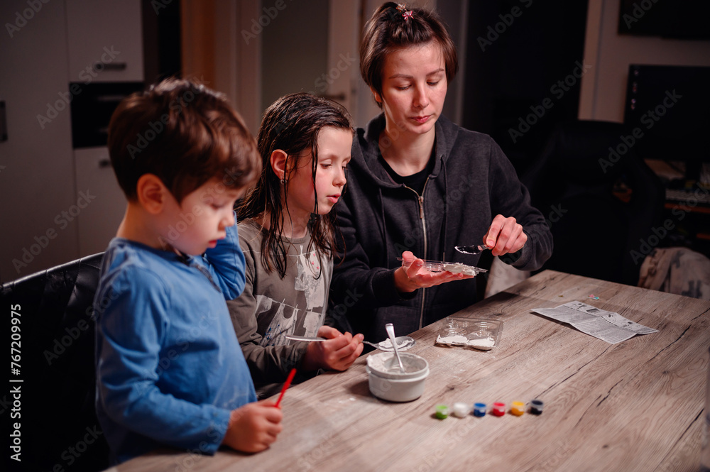 Focused siblings engage in a chemistry experiment with the help of a young woman, depicting a scene of shared learning and family bonding at home Focused siblings engage in a chemistry experiment with the help of a young woman, depicting a scene of shared learning and family bonding at home