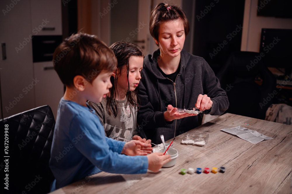 Focused siblings engage in a chemistry experiment with the help of a young woman, depicting a scene of shared learning and family bonding at home Focused siblings engage in a chemistry experiment with the help of a young woman, depicting a scene of shared learning and family bonding at home