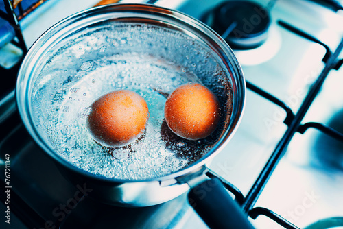 Saucepan stainless steel with two boiling eggs breakfast in a water on a gas stove top view.