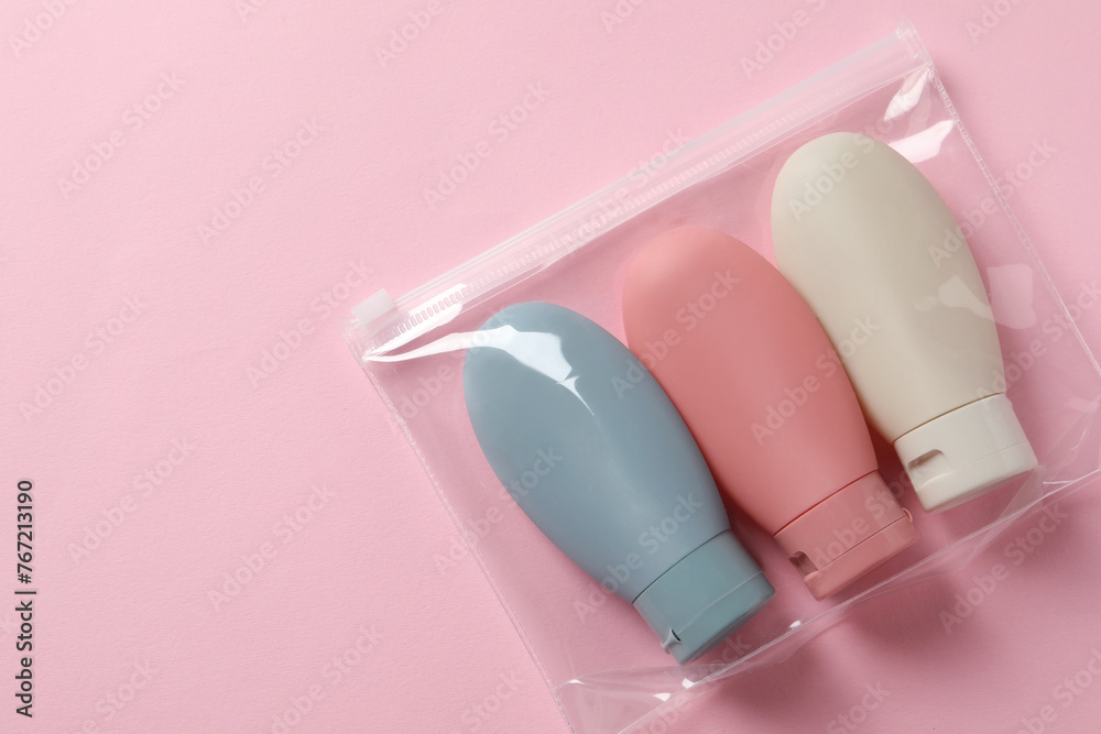 Obraz premium Cosmetic travel kit in plastic bag on pink background, top view. Space for text