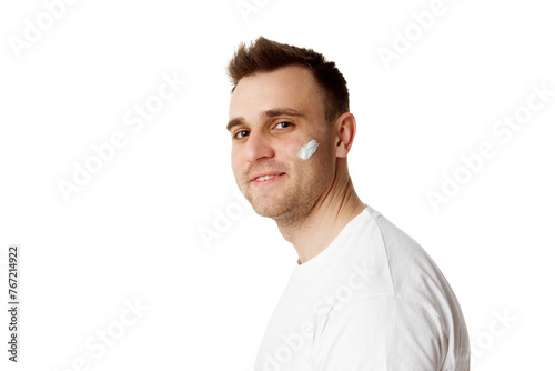 Smiling young, handsome man with facial care, moisturized cream looking at camera against white studio background. Concept of natural beauty, spa treatments, masculine, cosmetology.